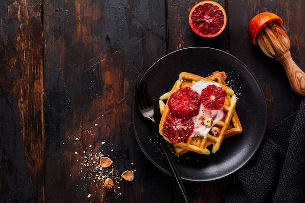 Waffles with yogurt and red Sicilian orange sauce on old dark wooden surface. Top view.