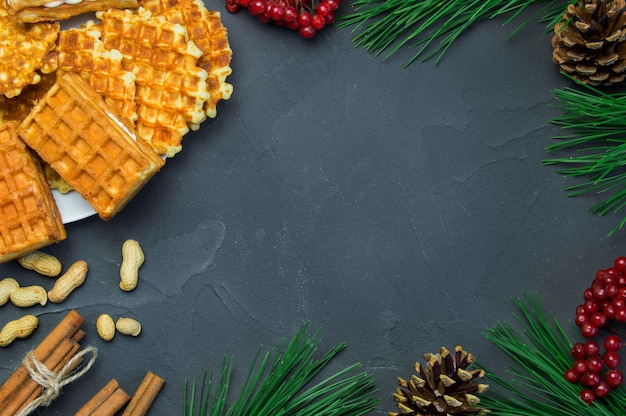 Wafle, peanuts and cinnamon sticks, branch christmas tree and ashberry with cone on dark rustic concrete surface