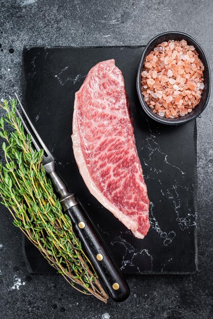 Wagyu raw sirloin steak, kobe beef meat on marble board. Black background. Top view.