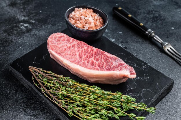 Wagyu raw sirloin steak, kobe beef meat on marble board. Black background. Top view.