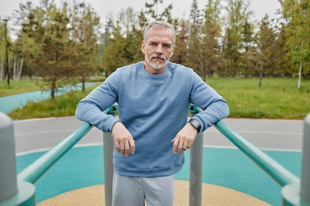 Waist up portrait of active mature man exercising on parallel bars outdoors and looking at camera co