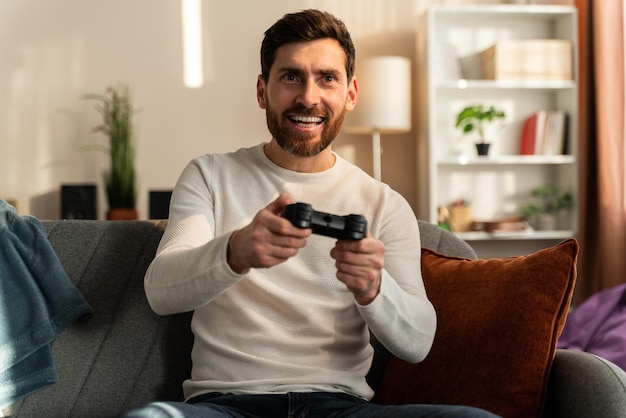 Waist up portrait of the bearded caucasian man with joystick playing video game alone on the couch. Stock photo