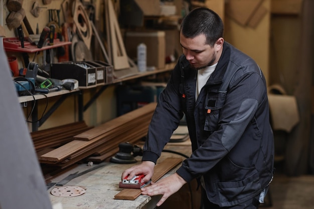 Waist up portrait of caucasian male worker sanding wood plank in workshop