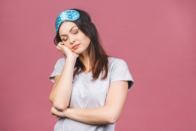 Waist up portrait of cheerful smiling girl in sleeping mask. Attractive funny female in stylish pajama standing and looking away. Isolated on pink background.