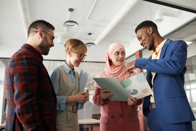 Waist up portrait of contemporary multi-ethnic team discussing business project in office, focus on Muslim businesswoman talking to colleagues