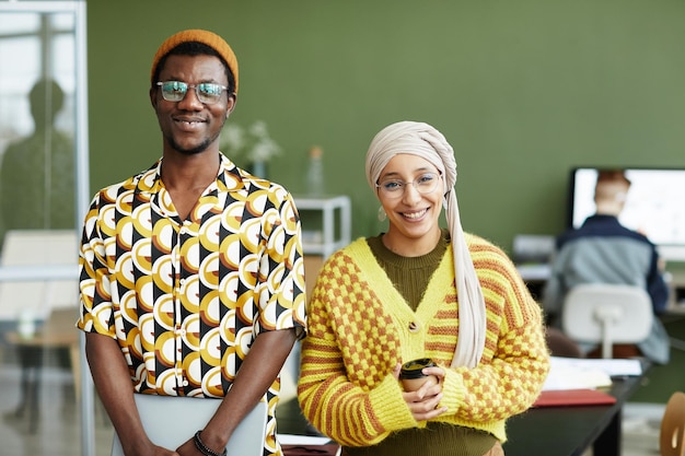 Waist up portrait of ethnic young couple wearing vibrant styles and smiling at camera in office