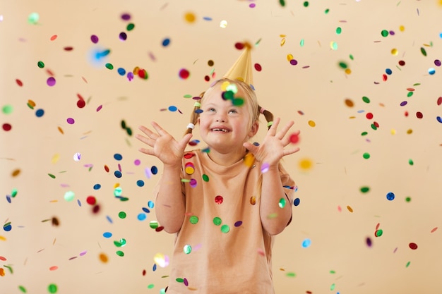 Waist up portrait of excited girl with down syndrome smiling happily while standing under confetti shower in studio, copy space