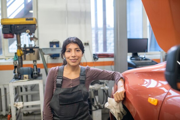 Waist up portrait of female mechanic looking at camera while standing by car in auto repair shop, copy space