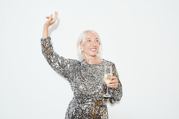 Waist up portrait of glamorous mature woman dancing against white background at party, shot with flash