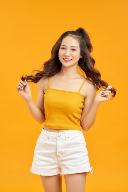 Waist up portrait of happy asian girl  smiling broadly looking at camera posing against yellow studio wall