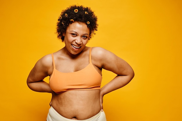 Waist up portrait of happy black woman with flowers in hair smiling at camera against vibrant yellow