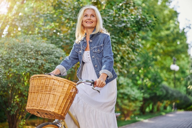 Подняв талию портрет счастливой смеющейся женщины, едущей на своем старинном велосипеде по летнему зеленому городскому бульвару