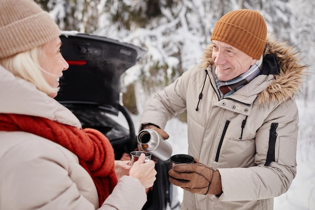 Waist up portrait of happy mature couple enjoying cup of hot coco outdoors in winter