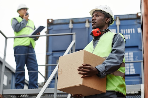 Photo waist up portrait of male african american worker carrying boxes up stairs at shipping docks