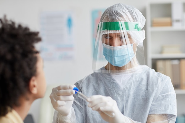 Waist up portrait of male doctor wearing full protective gear doing covid swab test in clinic, copy space