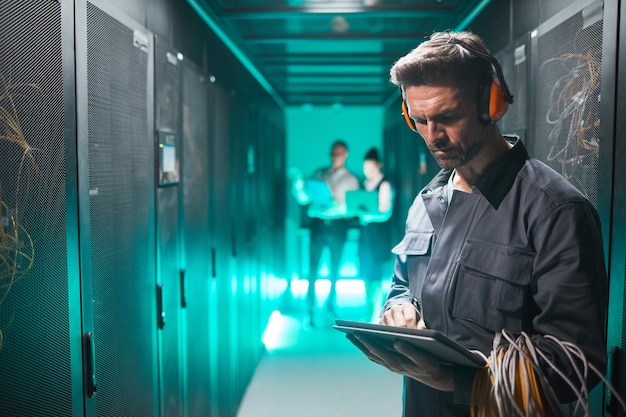 Photo waist up portrait of network engineer using tablet in server room during maintenance work in data center, copy space