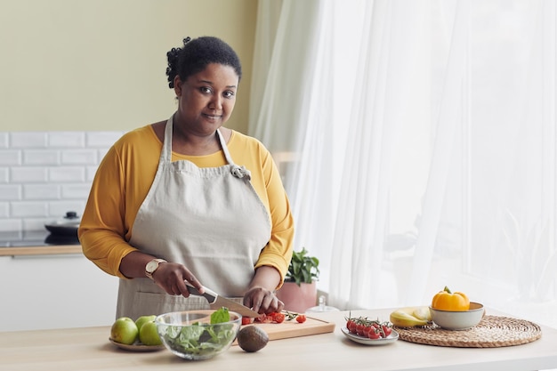 キッチンで健康的なサラダを調理し、カメラ コピー s を見て若い黒人女性の上半身の肖像画
