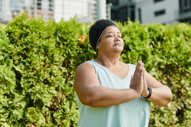 Waist up portrait of overweight mature woman holding hands together and medtating outdoors copy spac