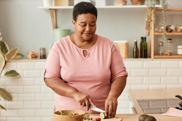 Waist up portrait of senior black woman cutting vegetables while cooking in cozy home kitchencopy sp