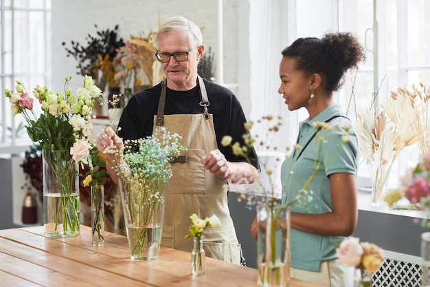 Waist up portrait of senior man consulting young woman while working in flower shop