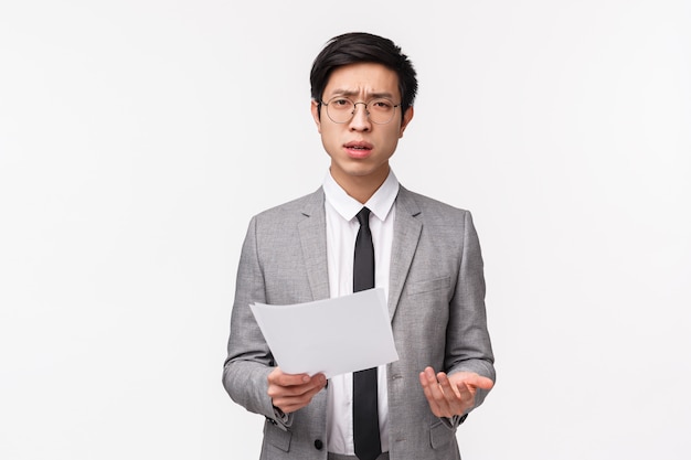 Waist-up portrait of skeptical, serious-looking asian businessman scolding employee for strange bad report