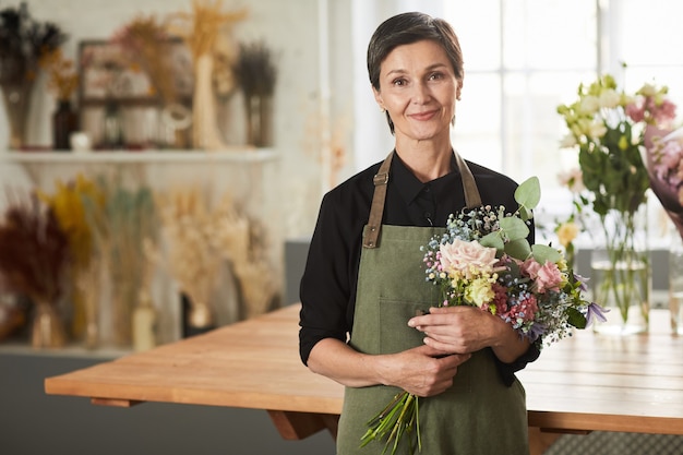 Foto mezzo busto ritratto di donna adulta sorridente che tiene i fiori in un negozio di fiori e guarda la copia della macchina...