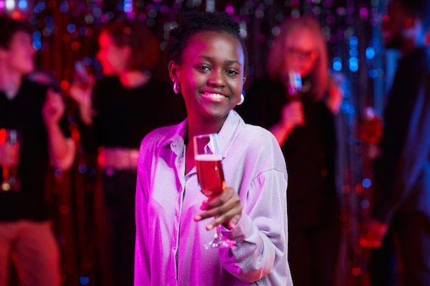 Waist up portrait of smiling African American woman holding drink at party in neon lights copy space