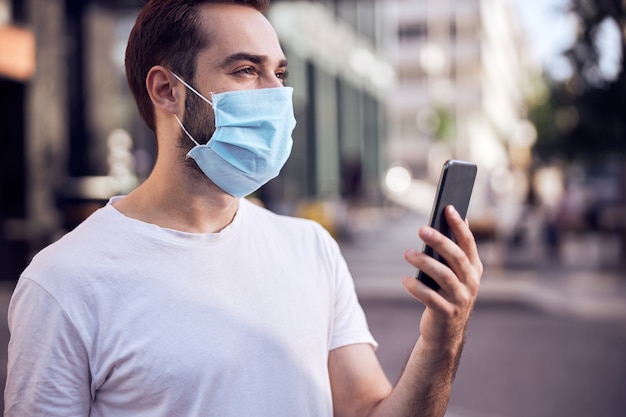 Waist up portrait of smiling man in mask with smartphone outdoors close up