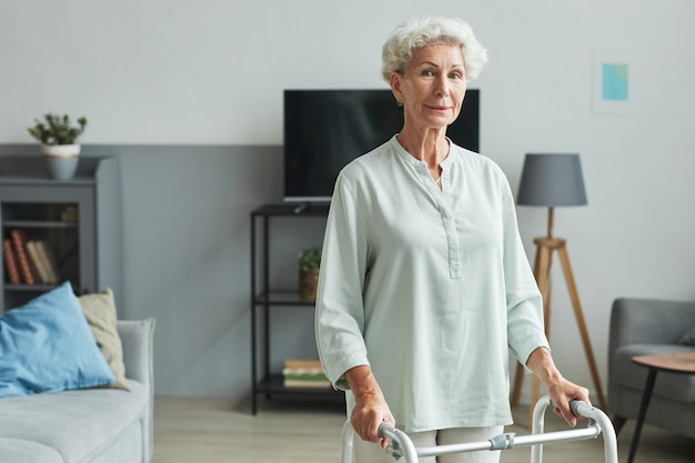 Waist up portrait of smiling senior woman using mobility walker in retirement home cop space