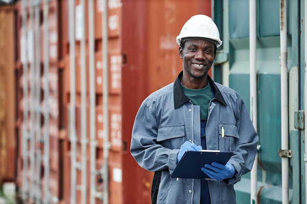 Photo waist up portrait of smiling young worker wearing hardhat while posing in container shipping docks c