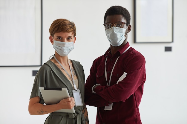 Waist up portrait of tattooed young woman posing with African-American man both wearing masks while planning art gallery exhibition, 