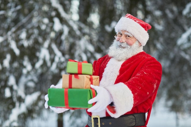 Ritratto in vita del tradizionale babbo natale che tiene una pila di regali all'aperto nel poliziotto della foresta invernale