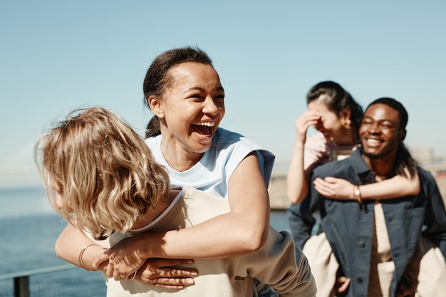 Waist up portrait of two carefree young couples having fun outdoors in Summer, focus on laughing young woman in foreground