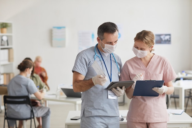 마스크를 쓰고 의료 클리닉에서 태블릿을 보면서 이야기하는 두 의사의 허리 초상화, 복사 공간