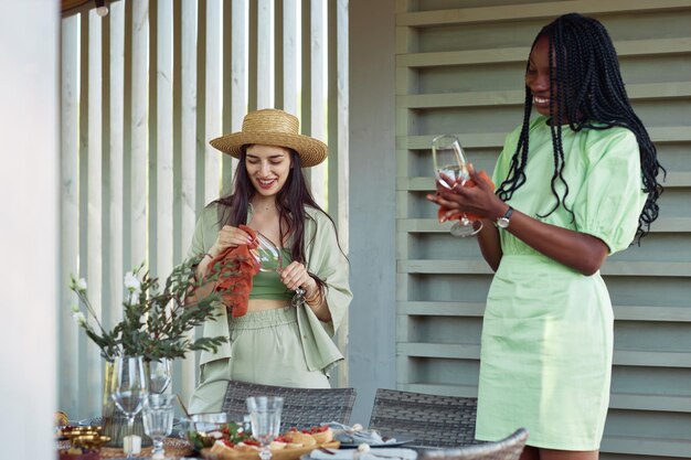 Waist up portrait of two young women setting up dinner table for party with friends outdoors in mute