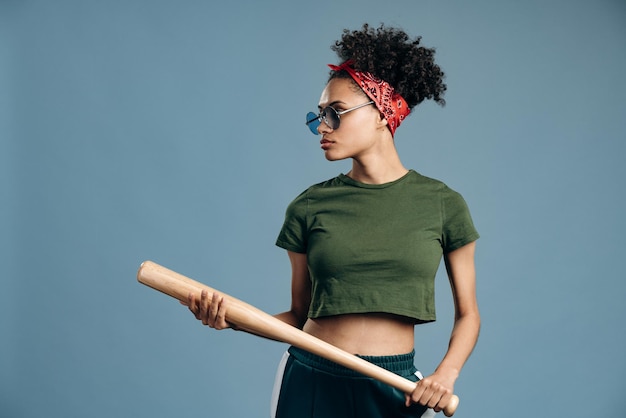 Waist up portrait view of the brutal woman wearing sunglasses holding baseball bat and looking away with serious emotion. Self-defense concept