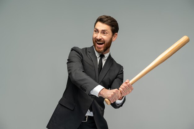 Waist up portrait view of the caucasian businessman swings with a baseball bat standing over grey background Occupation concept