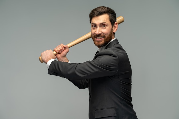 Waist up portrait view of the caucasian businessman swings with a baseball bat standing over grey background Occupation concept