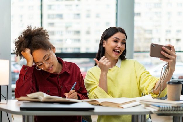 Waist up portrait view of the caucasian overjoyed woman gesturing while making selfie with her multiracial classmate Studying concept