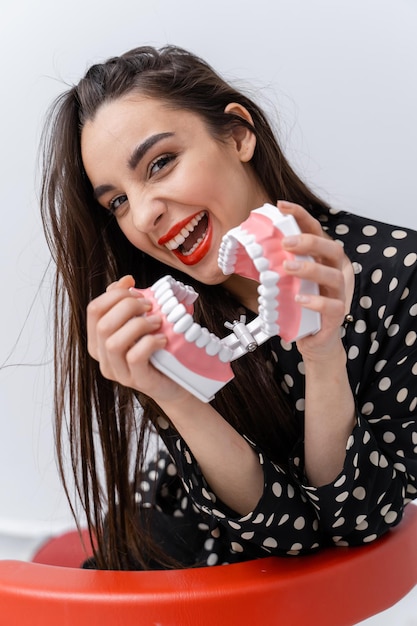 Waist up portrait view of the smile attractive woman with denture. Beautiful young female showing teeth, smiling while holding teeth model