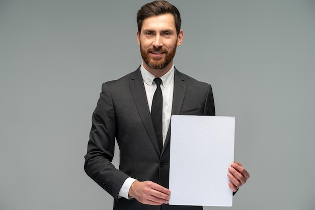 Waist up portrait view of the young businessman wearing suit holding blank paper while posing to the camera Business concept