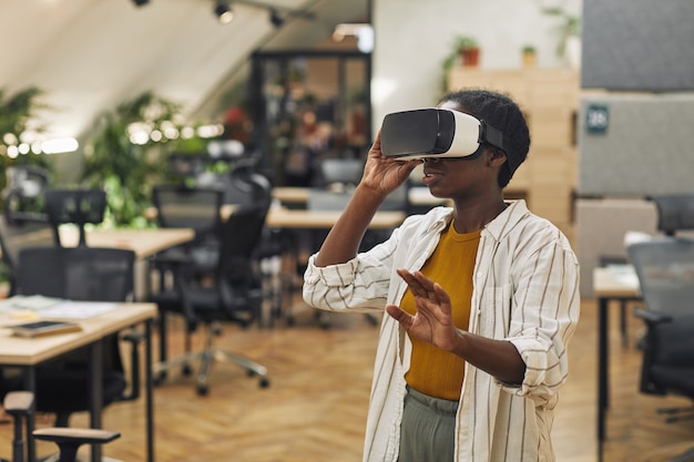 Waist up portrait of young African-America woman wearing VR helmet in office and enjoying immersive reality, copy space