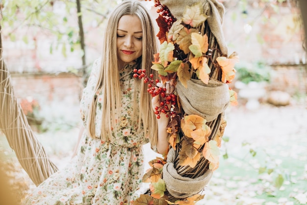 Waist up portrait of the young blonde beautiful caucasian woman sitting in big autumn wreath or swing and looking away while posing