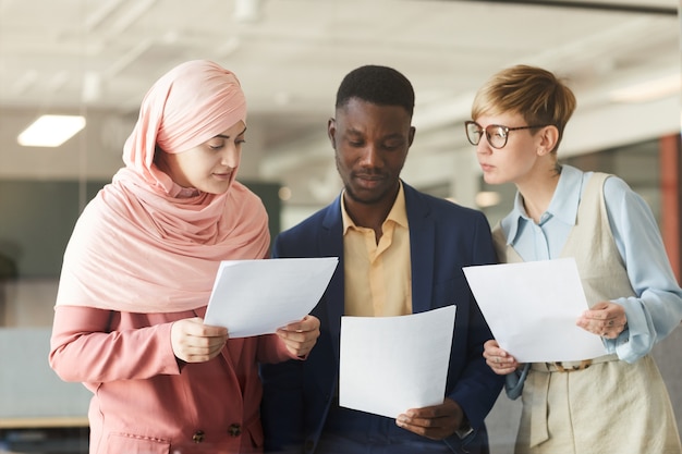 Waist up portrait of young multi-ethnic business team holding documents while discussing work project in office