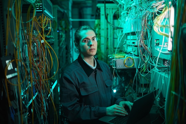 Waist up portrait of young network technician looking at camera in server room while setting up supercomputer in data center