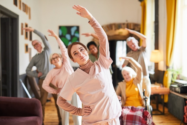 Waist up portrait young woman coordinating group of senior people enjoying morning exercises in reti...