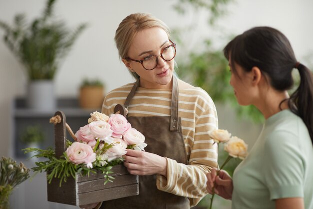 waist up portrait of young woman giving bouquet to customer while working in flower shop
