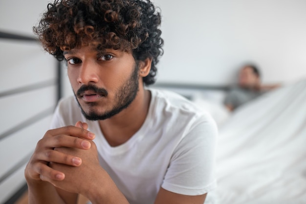 Foto vita in su di un uomo dai capelli ricci triste seduto con una faccia infelice