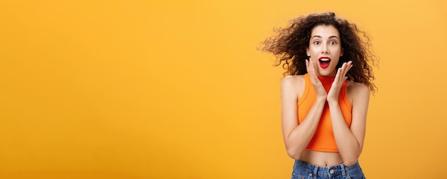 Waist-up shot of charmed enthusiastic attractive female with curly hairstyle in cropped top holding