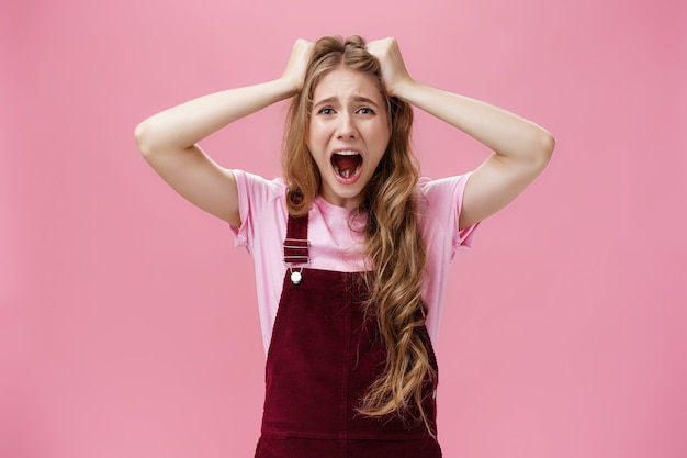 Foto colpo in vita di una donna in preda al panico che urla e tira i capelli fuori dalla testa facendo smorfie sentendo ansia da stress e problemi in piedi infastiditi e angosciati su sfondo rosa. copia spazio